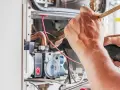 Tecnico che lavora su un **scambiatore acqua calda**, pulendo componenti interni con un pennello e un aspiratore.