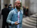 Hombre calvo sin barba, con auriculares y chaqueta vaquera, mira su móvil.
