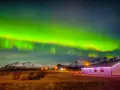 Islandia pogoda listopad: zorza polarna nad ośnieżonymi górami i domkiem z lampkami.