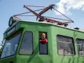Uśmiechnięty mężczyzna w czerwonym swetrze wygląda z okna zielonej lokomotywy. To łódź Skierniewice, gotowa do podróży.
