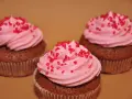 Tre chokladmuffins med rosa frosting och röda strössel, bakade i rosa muffinsformar.