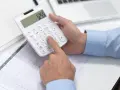 Persona calculando en calculadora blanca, revisando documentos y tablet. Se pregunta cuánto cuesta abrir una empresa en España.