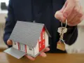 Mano ofrece maqueta de casa y llaves, símbolo de propiedad y seguridad ante la ley antiokupas.