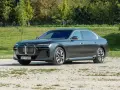 Elegancki, grafitowy BMW 740d na tle zieleni. Luksusowa limuzyna prezentuje się imponująco.