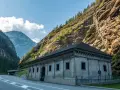 Edificio in pietra ai piedi di una montagna rocciosa, con strada e tunnel. Un passo alpino che sembra non finire mai, un vero sempione passo.