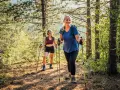 Deux femmes souriantes randonnent en forêt, utilisant des bâtons. Elles semblent apprécier la nature, un argument pour ou contre les bâtons de randonnée.