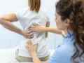 Fizjoterapeuta bada plecy pacjentki. Po długiej rehabilitacji wreszcie wyleczyłem kręgozmyk i czuję się znacznie lepiej.