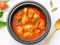 Pollo en salsa de tomate casera en olla negra, con hojas de laurel y perejil picado.