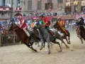 Jockeys in colorful silks race horses during the Palio di Siena. Dust flies as the horses thunder across the track, a thrilling spectacle of the historic siena horse race.