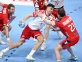 Gracz w białej koszulce z numerem 9 próbuje rzucić piłkę, podczas gdy obrońca w czerwonej koszulce z numerem 23 stara się mu przeszkodzić. Emocjonująca akcja w meczu piłki ręcznej.