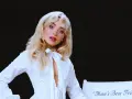 Sabrina Carpenter w białej koszuli, z rozpuszczonymi blond włosami, wygląda jak "man's best friend" na tle czerni.