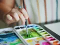 Main d'une artiste, bague turquoise, tenant un pinceau au-dessus d'une palette de couleurs vives de **de l'aquarelle**.