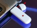 Biały modem USB podłączony do laptopa, umożliwiający komórkową transmisję danych.