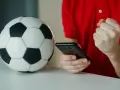 Piłka nożna i smartfon. Kibic sprawdza wynik, licząc na powyżej 2.5 gola.