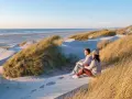 Ett par sitter på en sanddyn och njuter av utsikten över havet. Vackra sanddyner med gräs sträcker sig längs kusten, en idyllisk plats i en nationalpark i Danmark.