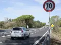 Un'auto bianca percorre una strada extraurbana secondaria, superando un cartello di limite di velocità a 70 km/h.