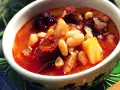 Un cuenco de alubias con trozos de chorizo, morcilla y patata en un caldo rojizo.
