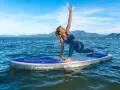 Frau praktiziert Krieger II auf einem SUP-Board auf ruhigem Wasser, Berge im Hintergrund.