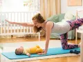 Mama wykonuje ćwiczenia po porodzie na macie, a jej maluch leży obok.