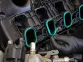 A gloved hand installs a new intake manifold gasket, ensuring a tight seal for optimal engine performance.