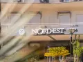 Hotel Nord Est sign with a compass logo and five stars, framed by palm fronds.