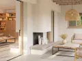 Salón luminoso con chimenea de piedra, muebles de madera y textiles naturales, evocando un relajante estilo ibicenco.
