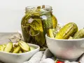 Cetrioli in agrodolce in un barattolo di vetro e in ciotole, con aglio e spezie.