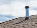 Cheminée tubée sur un toit, sous un ciel bleu et nuageux. Une aide financière pour le tubage de cheminée pourrait être nécessaire pour ce type d'installation.