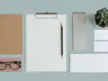 Un bureau minimaliste avec un carnet, des lunettes, un presse-papiers, un crayon, un carnet, une plante et des cartes de visite. Un exemple de book artistique.