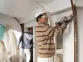 Un ouvrier en train d'enduire un mur abîmé avec soin. Un autre ouvrier travaille en arrière-plan.