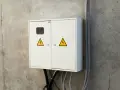 Biała skrzynka elektryczna na betonie z symbolami ostrzegawczymi. Przydatna przy wypełnianiu wniosku o określenie warunków przyłączenia PGE wzór.