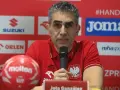 Jota González, trener reprezentacji Polski w piłce ręcznej, przemawia do mikrofonu. Obok niego czerwona piłka.