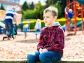 Chłopiec z zespołem Aspergera siedzi samotnie na placu zabaw, podczas gdy inne dzieci się bawią.