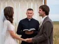 Ksiądz na ślubie, trzymając otwartą księgę, błogosławi parę młodą.