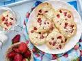 Saftige Erdbeer-Cookies mit weißen Schokostückchen auf einem Teller, daneben frische Erdbeeren und ein Glas Milch.