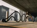 Un homme s'entraîne avec des cordes de bataille sous un pont. Il est concentré, ses muscles tendus. Les bienfaits de la glutamine pour la récupération sont essentiels pour ce type d'effort.