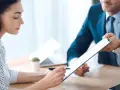 Kobieta podpisuje dokument na tablecie, mężczyzna w garniturze podaje jej go.