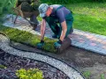 Ogrodnik układa trawę z rolki, tworząc piękny trawnik. Sprawdź atrakcyjną trawę z rolki cenę za m2!