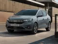 Szary Dacia Sandero, pierwszy samochód wielu rodzin, jedzie po miejskiej drodze.