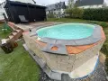 Ein Pool mit selbstgemachten Randsteinen, umgeben von Holz und Naturstein.