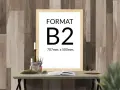 Ramka z napisem "FORMAT B2 707mm. x 500mm." na tle drewnianej ściany. Na stole obok książka i świece.