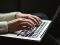 Dłonie piszą na laptopie. Ktoś przygotowuje wypowiedzenie umowy o pracę po angielsku, szukając wzoru.