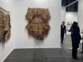Exposición de arte contemporáneo con tapices texturizados y personas observando.
