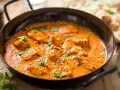 Aksamitny kurczak w sosie curry, udekorowany świeżą kolendrą, kusi aromatem. Obok widać kawałki chleba naan.