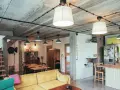 Nowoczesne wnętrze z widoczną instalacją elektryczną natynkową na betonowym suficie. Wygodna kanapa, stół jadalniany i kuchnia.