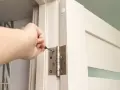 Dłoń dokręca śrubę zawiasu, montując drzwi ukryte w ścianie.