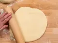 Hand rollt Teig auf Holzbrett aus. Vielleicht mit Dinkelmehl? Was ist Dinkelmehl?