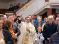 Kapłan błogosławi wiernych podczas liturgii Wielkiej Soboty, unosząc kropidło. W tłumie widać ludzi z zapalonymi świecami.