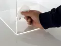 A hand applies adhesive to the corner of a clear plastic box, demonstrating precise gluing of plastic for a clean finish.