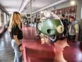 Un raduno moto Guzzi in un museo. Una moto da corsa verde con il numero 1 in primo piano, ammirata da visitatori.
